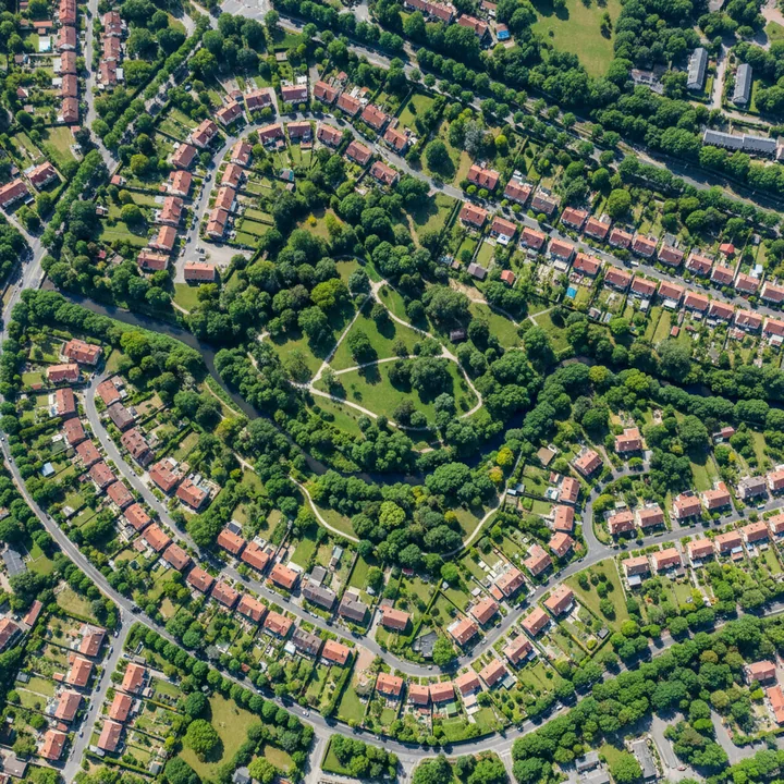 Widok z lotu ptaka na miasto‑ogród: przestrzenie między domami wypełnione drzewami, alejami i parkiem, gęsta zieleń otacza zabudowę
