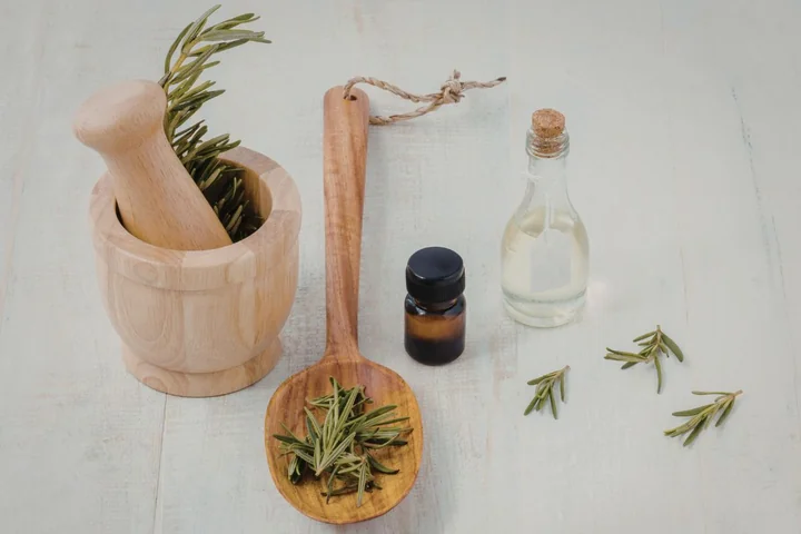 Moździerz i tłuczek z rozmarynem, drewniana łyżka z gałązkami, buteleczki olejków i rozmaryn na jasnym blacie