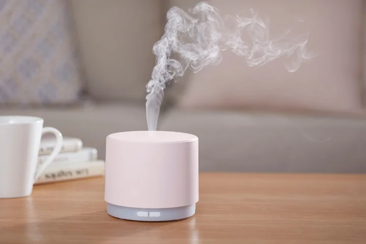 Różowy dyfuzor zapachowy na stole, unosząca się para i kubek z książkami w tle.