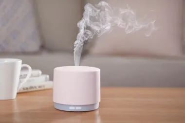 Różowy dyfuzor zapachowy na stole, unosząca się para i kubek z książkami w tle.