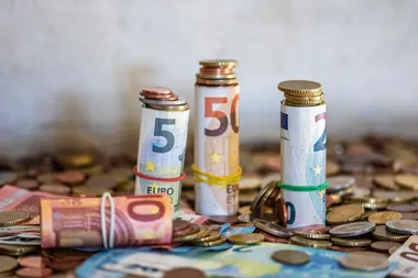 Rolki banknotów euro i stosy monet na stole.
