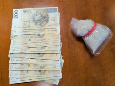 Na drewnianym blacie leży stos banknotów 200 złotych obok plastikowego woreczka z białą sypką substancją związanego różową gumką.