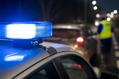 Nocna akcja drogowa policji: w pierwszym planie kogut świetlny radiowozu, w tle funkcjonariusz w kamizelce odblaskowej przy samochodzie na oświetlonej ulicy.
