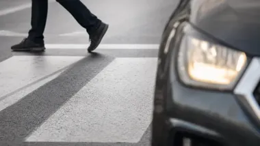Fragment samochodu na przejściu dla pieszych, w tle nogi pieszego przechodzącego przez przejście.